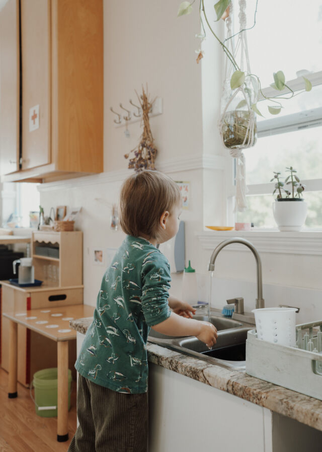 A toddler washes up at the classroom sink